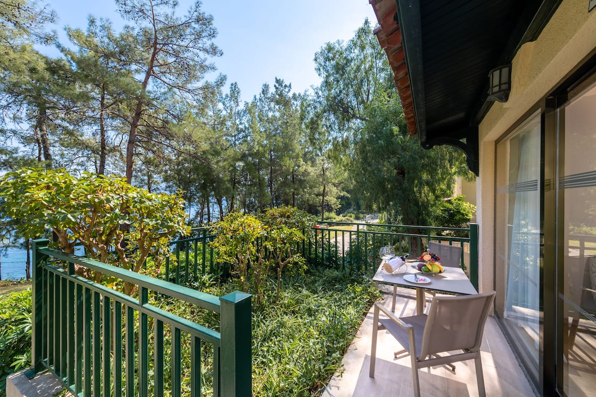 Varanda com mesa e cadeiras, vista para um corpo d'água e área arborizada.