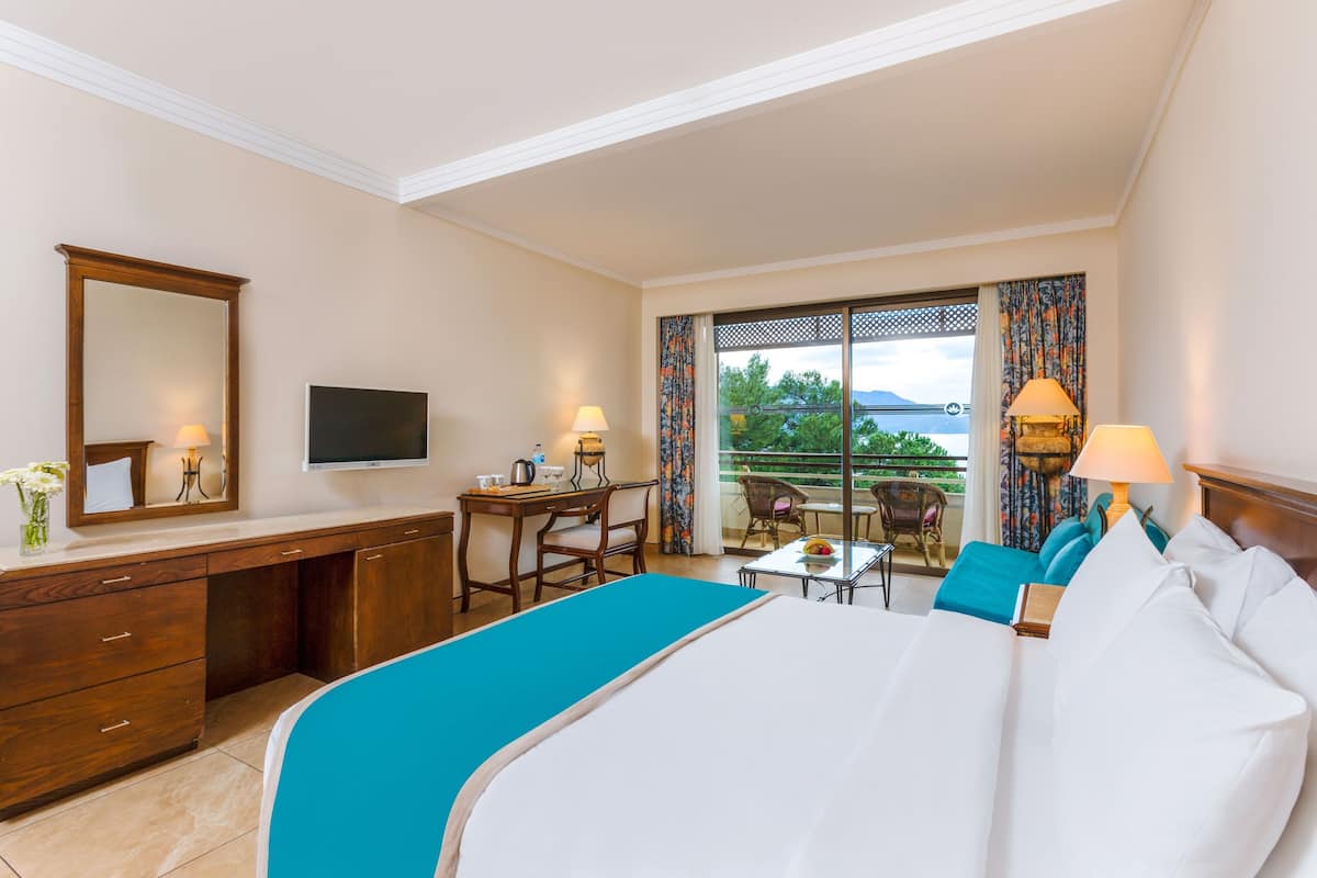 Quarto de hotel com uma cama grande, escrivaninha, cadeira, televisão e varanda com vista.