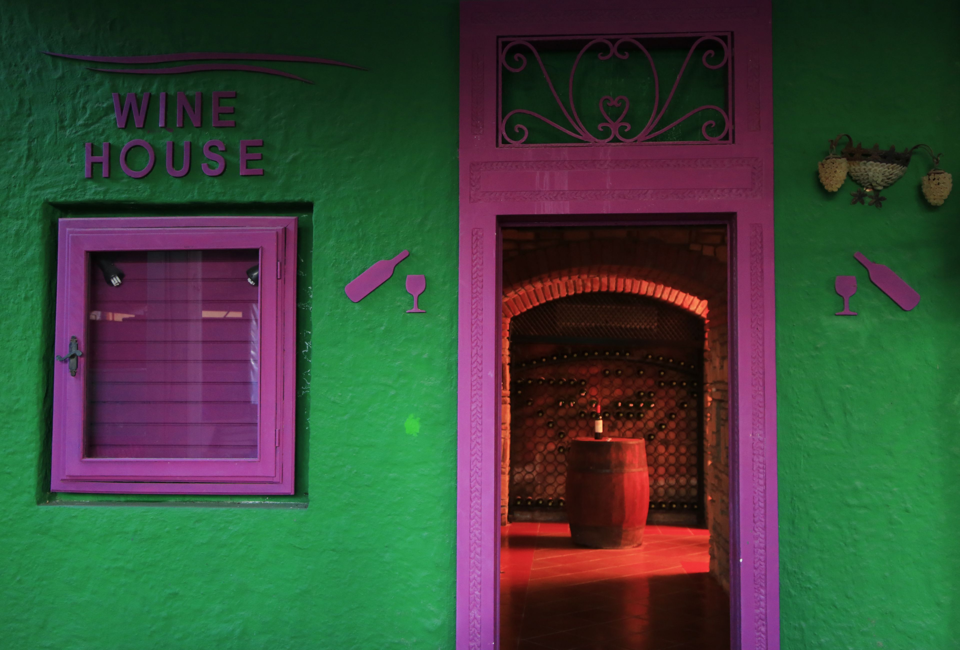 A wine cellar entrance with a wooden barrel, a wine bottle, and a wine glass decoration.