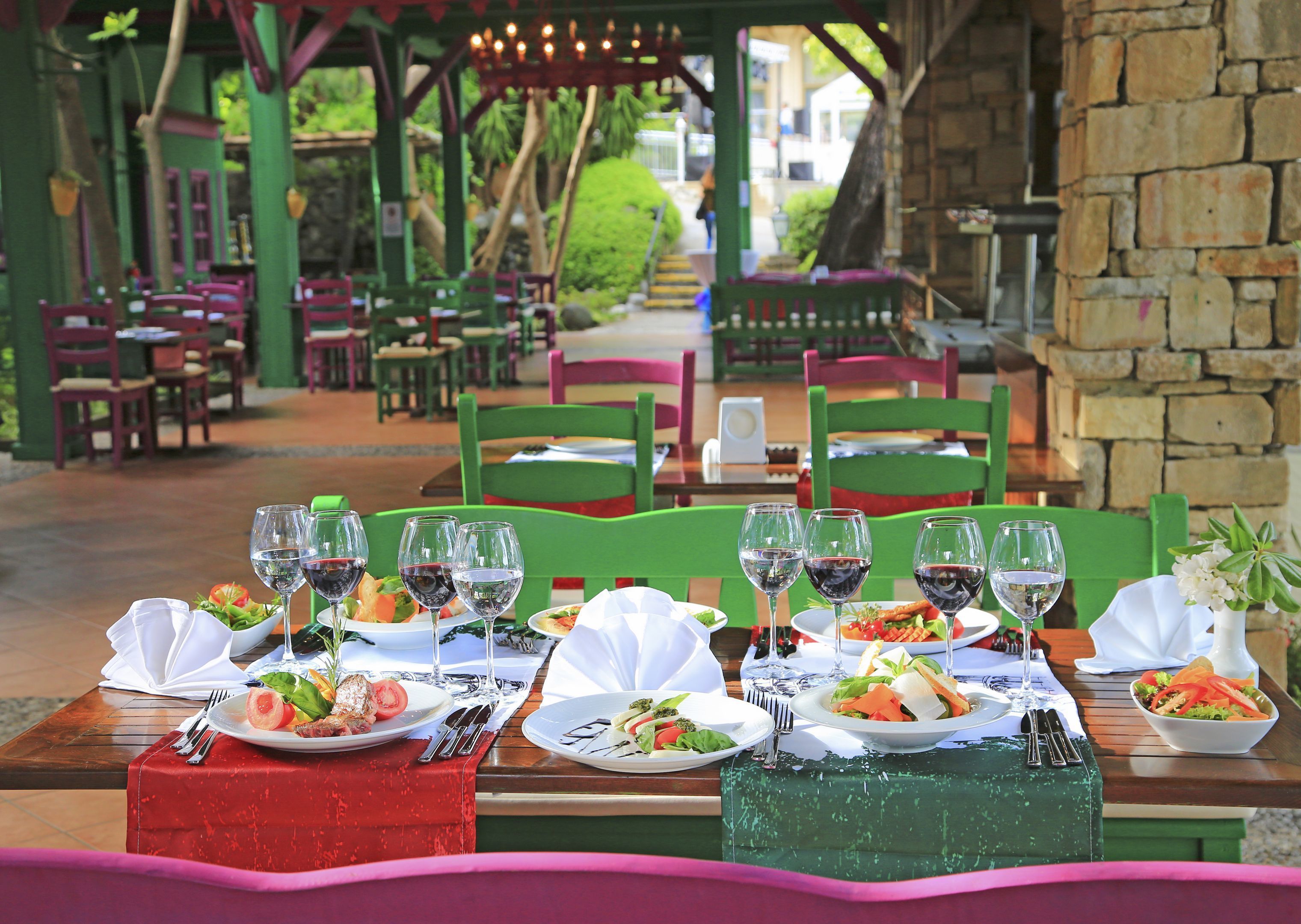 A restaurant with outdoor seating, green chairs, and tables set with plates of food and wine glasses.