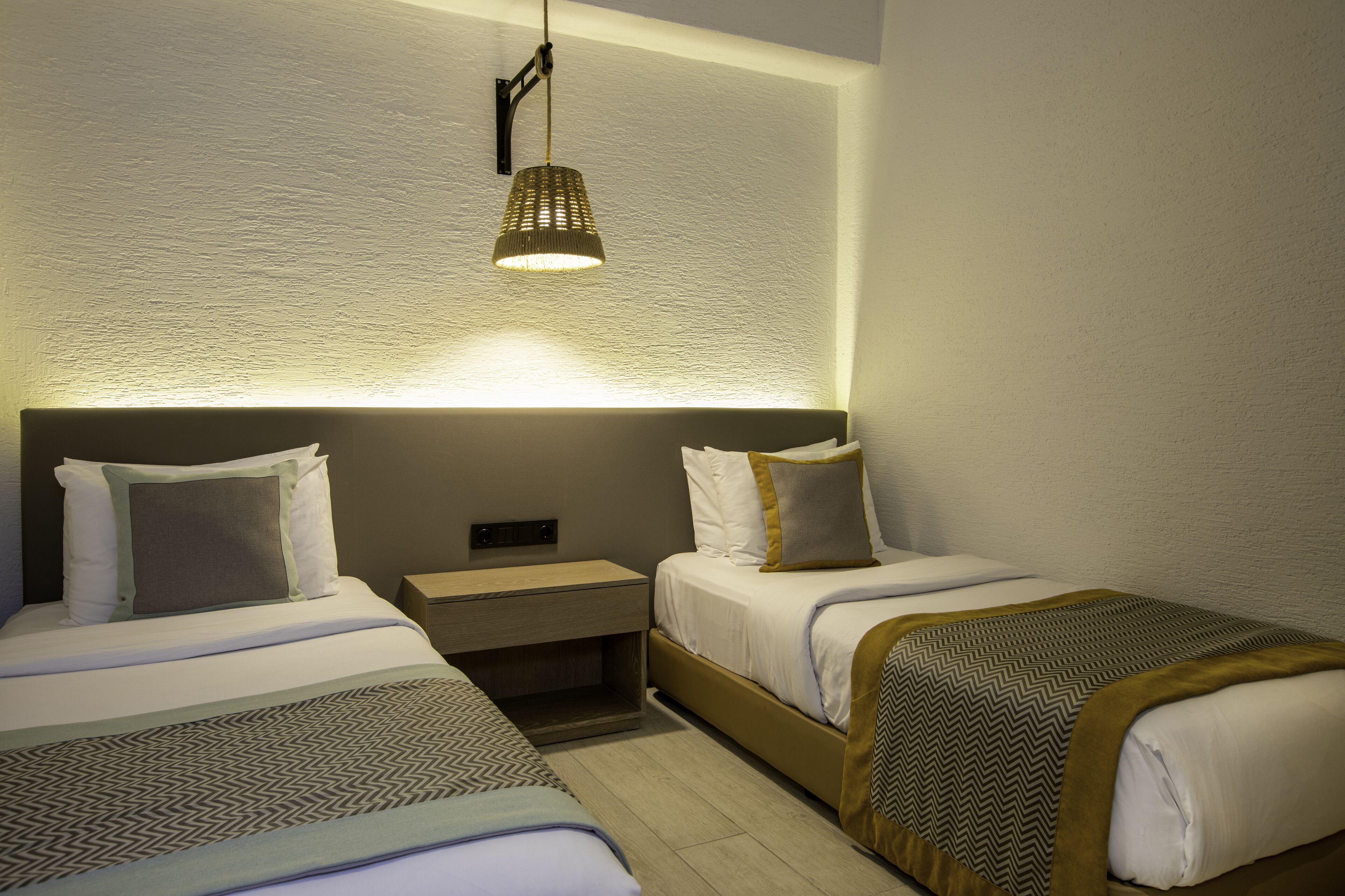 A hotel room with two beds, a nightstand, a lamp, and a textured wall.