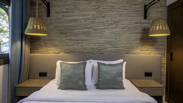 A neatly made bed with two pillows, a stone wall, and two hanging lamps.