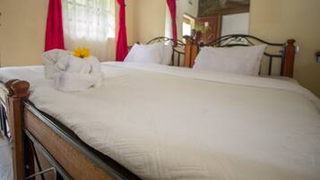 A neatly made bed with white linens and a yellow flower, red curtains, and a wooden headboard.