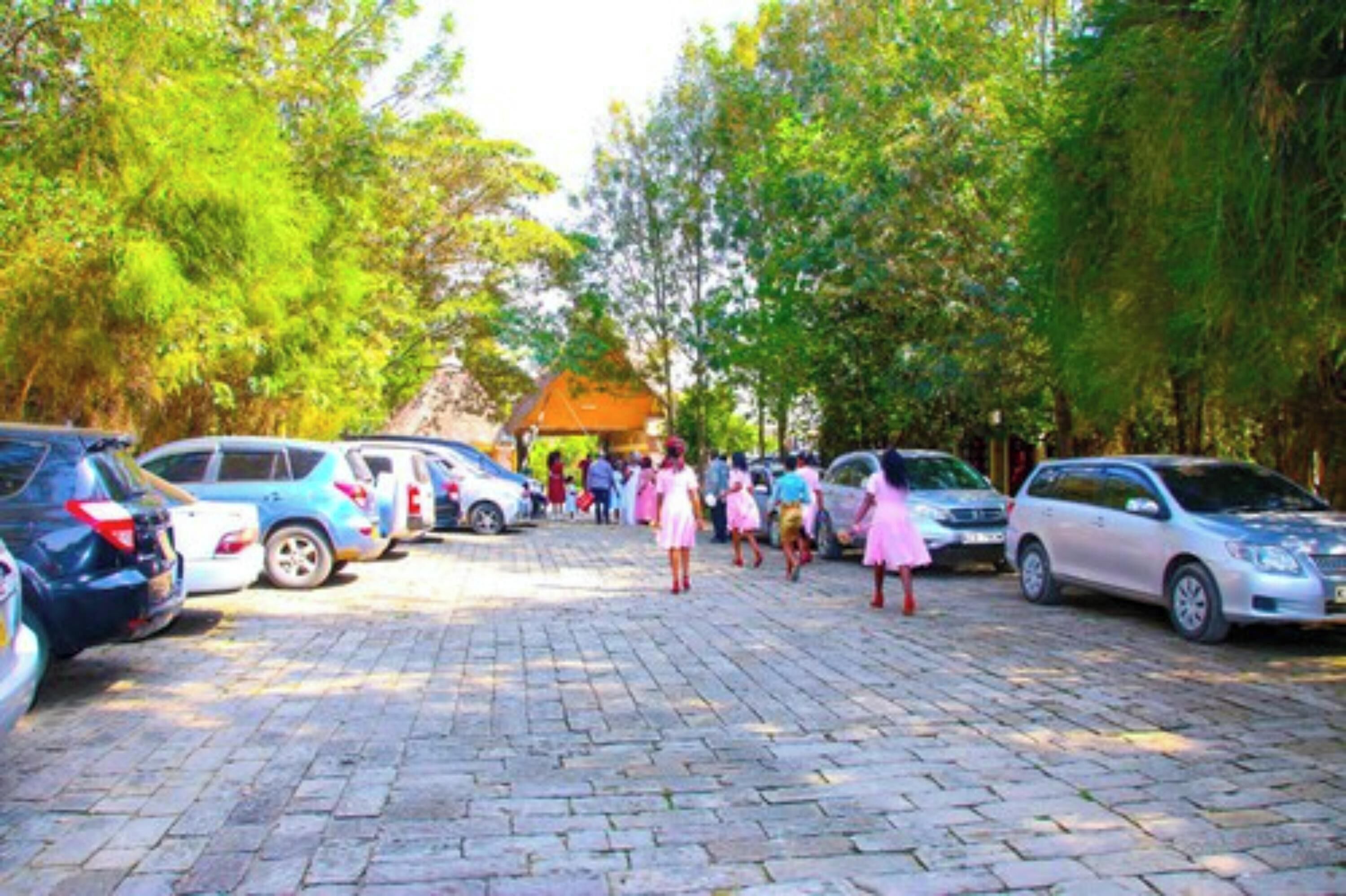 A paved parking area with cars and people walking.