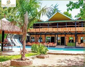A two-story lodge with a pool, surrounded by tropical vegetation.