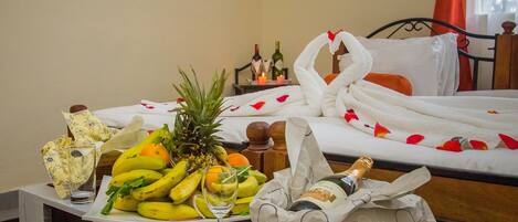 A neatly made bed with white linens and a bouquet of red flowers.