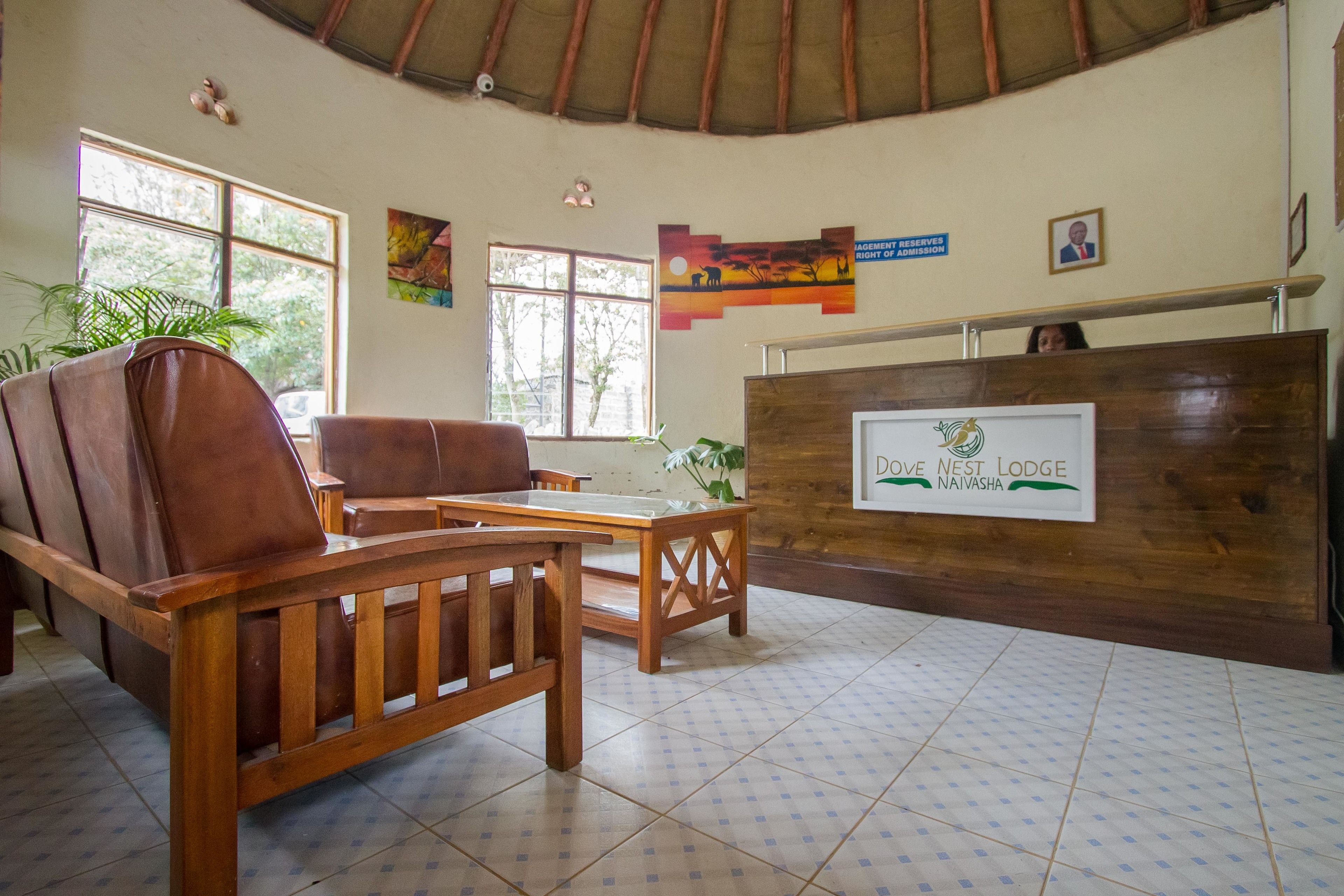 A reception area with wooden furniture, a tiled floor, and a sign for 'Love Nest Lodge Naivasha'.