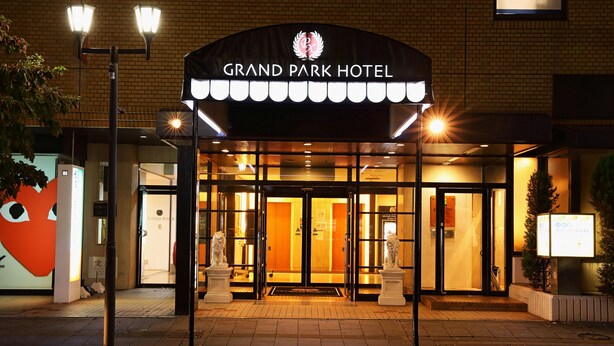 L’entrée du Grand Park Hotel se distingue par sa façade en briques, ses portes d’entrée illuminées et une enseigne placée au-dessus.