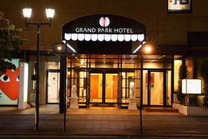 De ingang van het Grand Park Hotel met een bakstenen gevel, verlichte deuropeningen en een bord erboven.