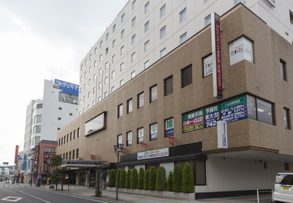 Een hotel met meerdere verdiepingen, een gevel van baksteen, verschillende borden met bedrijfsnamen en een parkeerplaats ervoor.