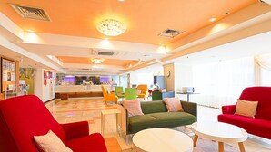 Un hall d’hôtel moderne doté d’un espace salon central, d’un comptoir d’accueil et d’une vue sur la réception.