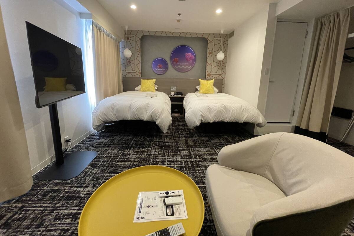 A hotel room with two beds, a TV, a sofa, and a tray table with a remote control.