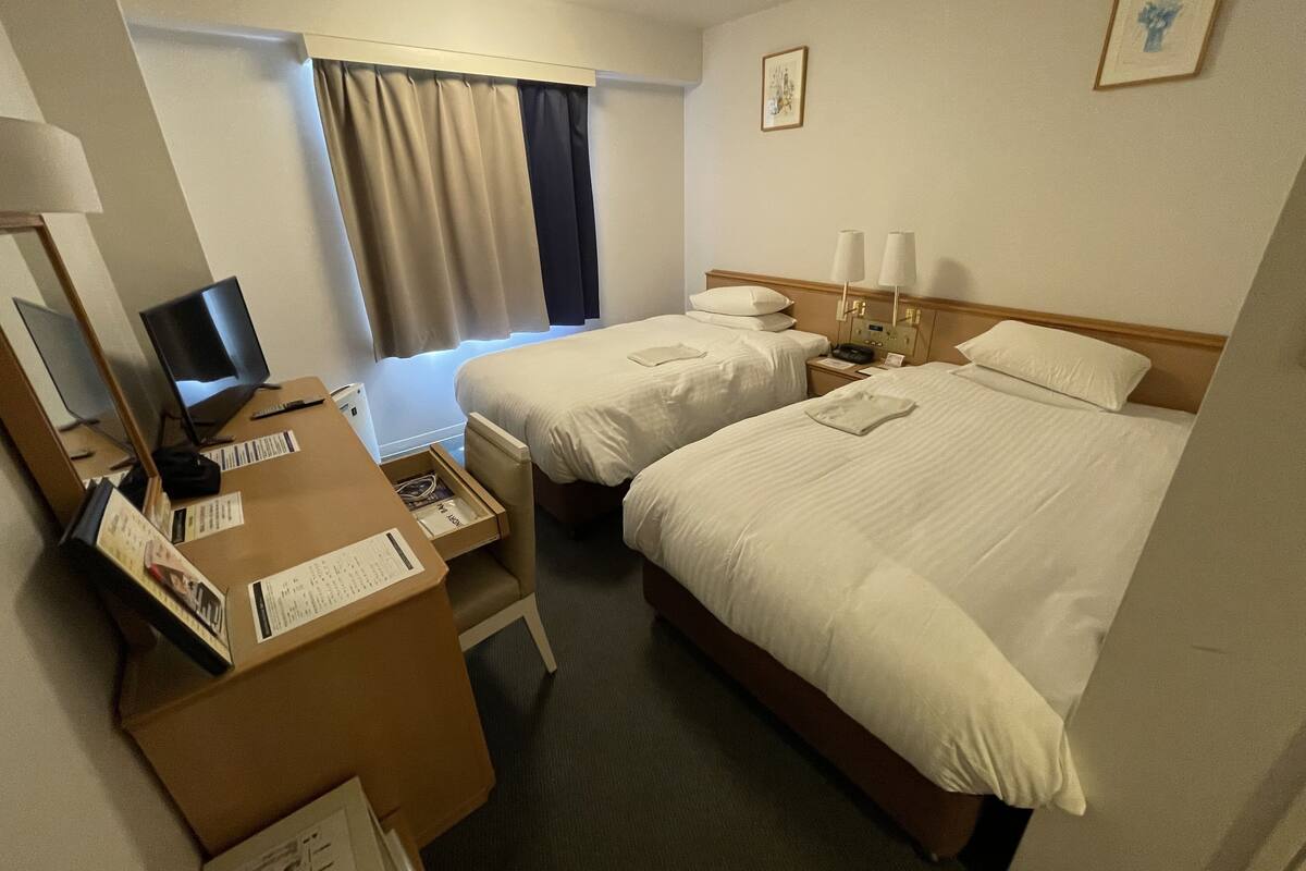 A hotel room with two beds, a desk with a computer, and a window with curtains.