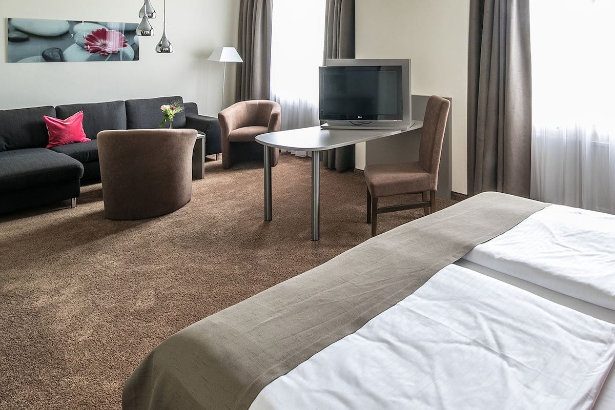 A hotel room with a bed, a desk with a TV, a sofa, and a chair.