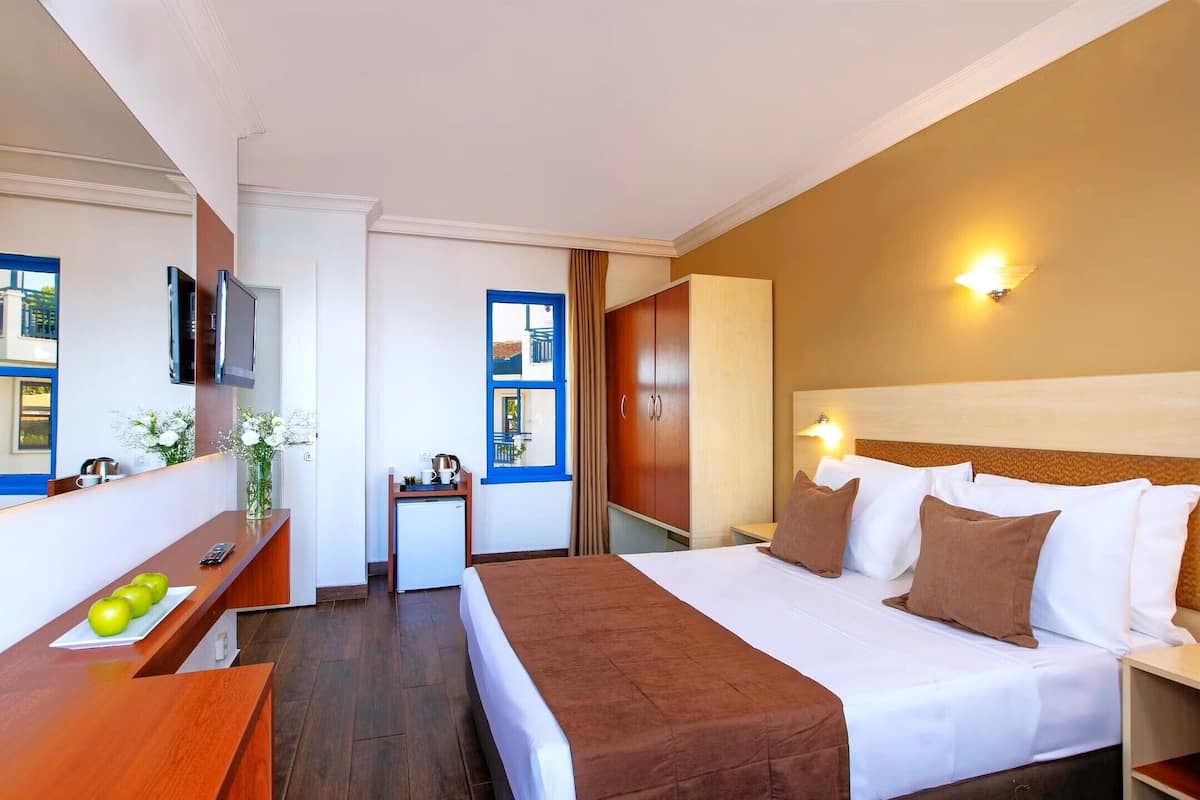A hotel room with a bed, a desk with a computer, a television, and a window with curtains.