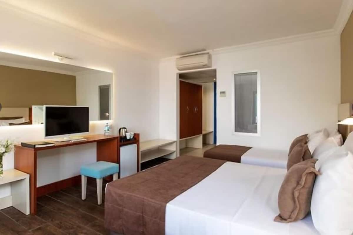 A hotel room with a bed, a desk, a chair, a television, and a small stool.