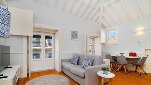 Una sala de estar moderna con un sofá gris, una mesita redonda y un televisor sobre un mueble blanco.