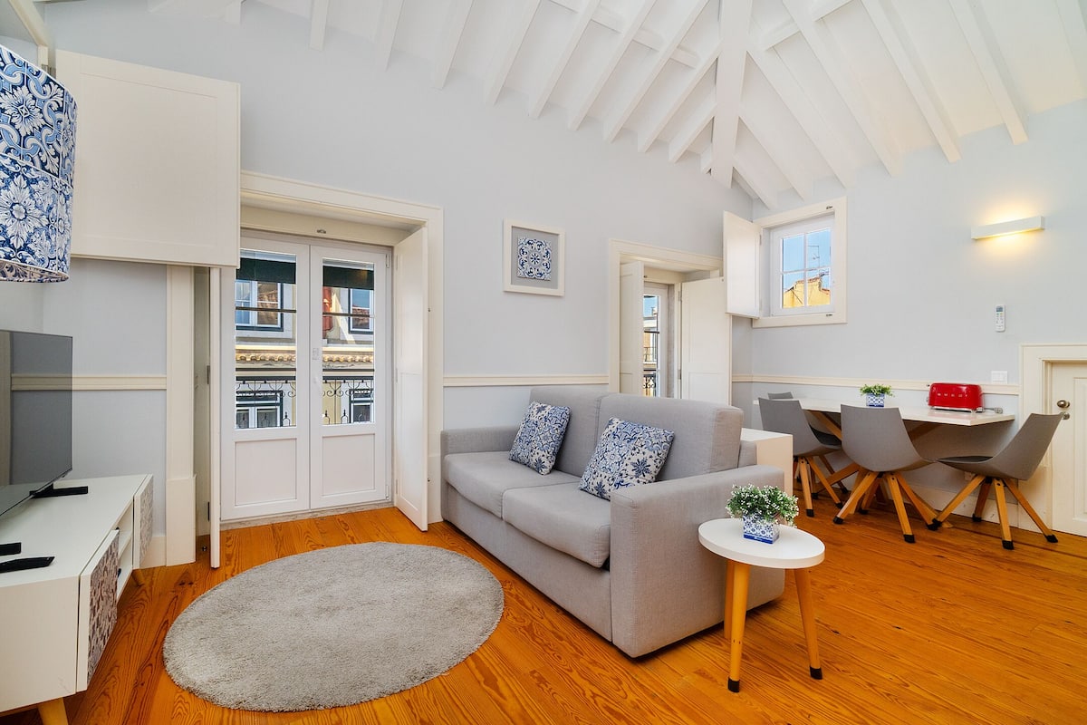 Una sala de estar moderna con un sofá gris, una mesita redonda y un televisor sobre un mueble blanco.