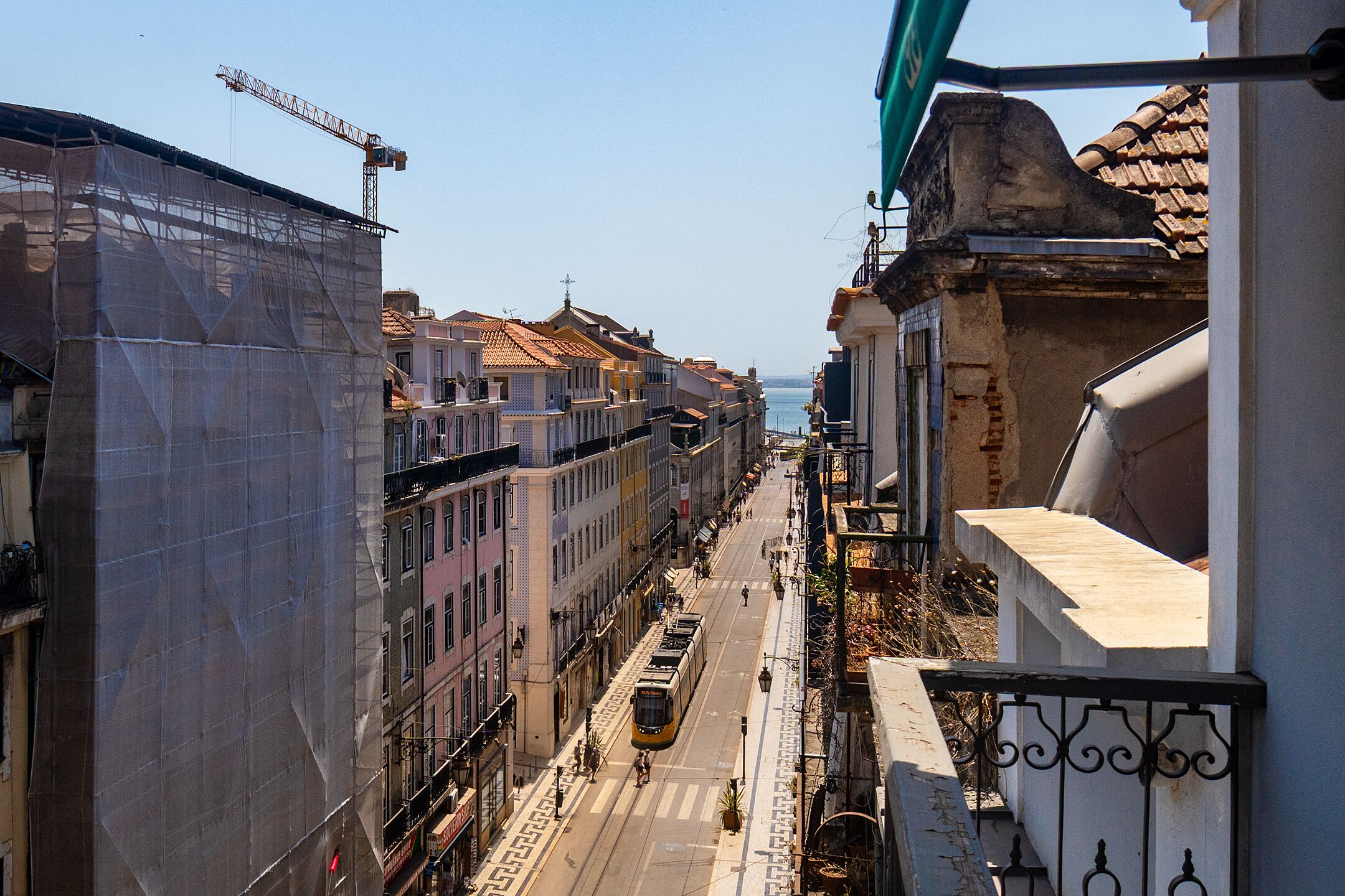 A narrow street with buildings on both sides, a tram, and a construction crane in the distance.