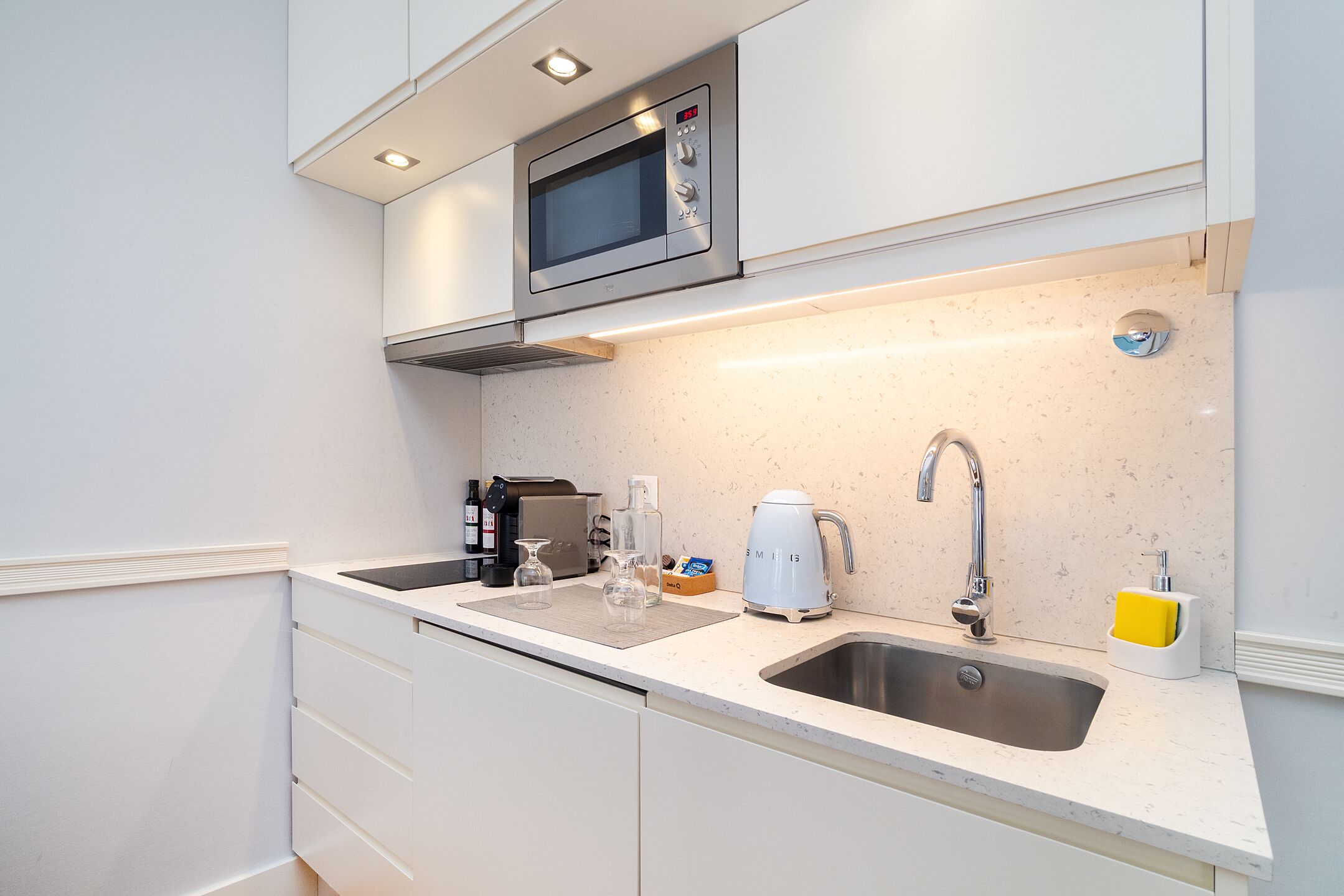 Cocina moderna con microondas, lavamanos y cafetera.