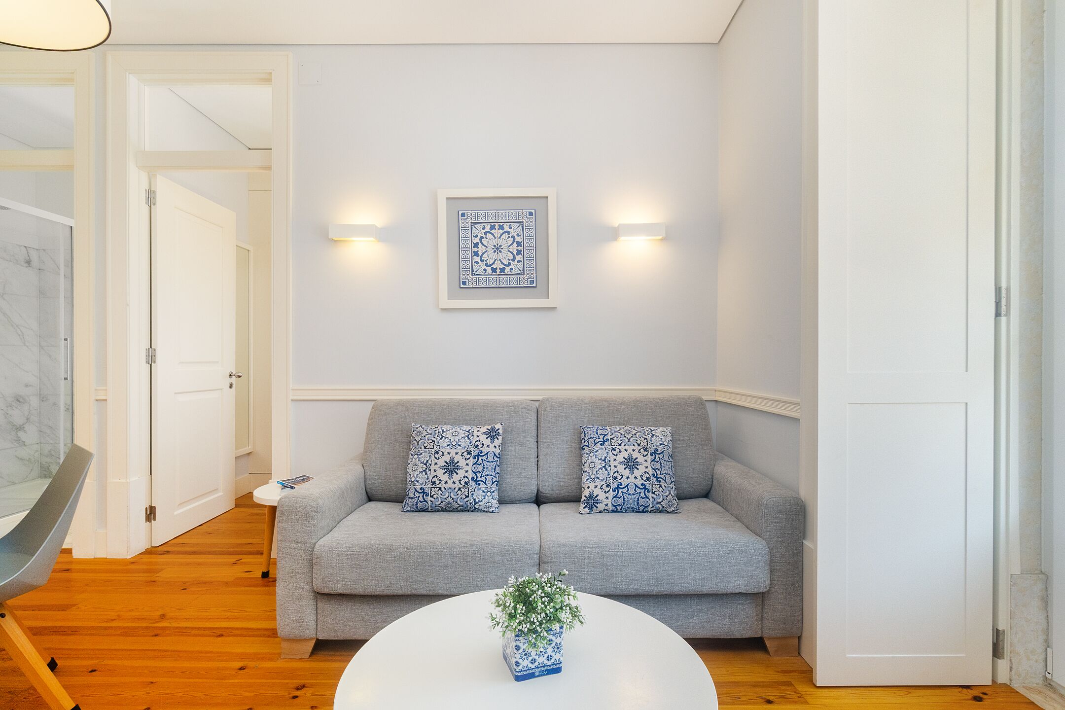 A modern living room with a grey sofa, two patterned throw pillows, a white coffee table with a plant, and a framed artwork on the wall.