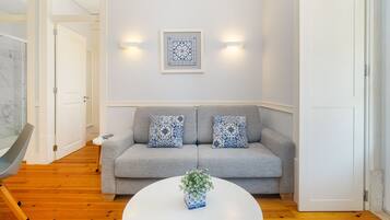 A modern living room with a grey sofa, two patterned throw pillows, a white coffee table with a plant, and a framed artwork on the wall.