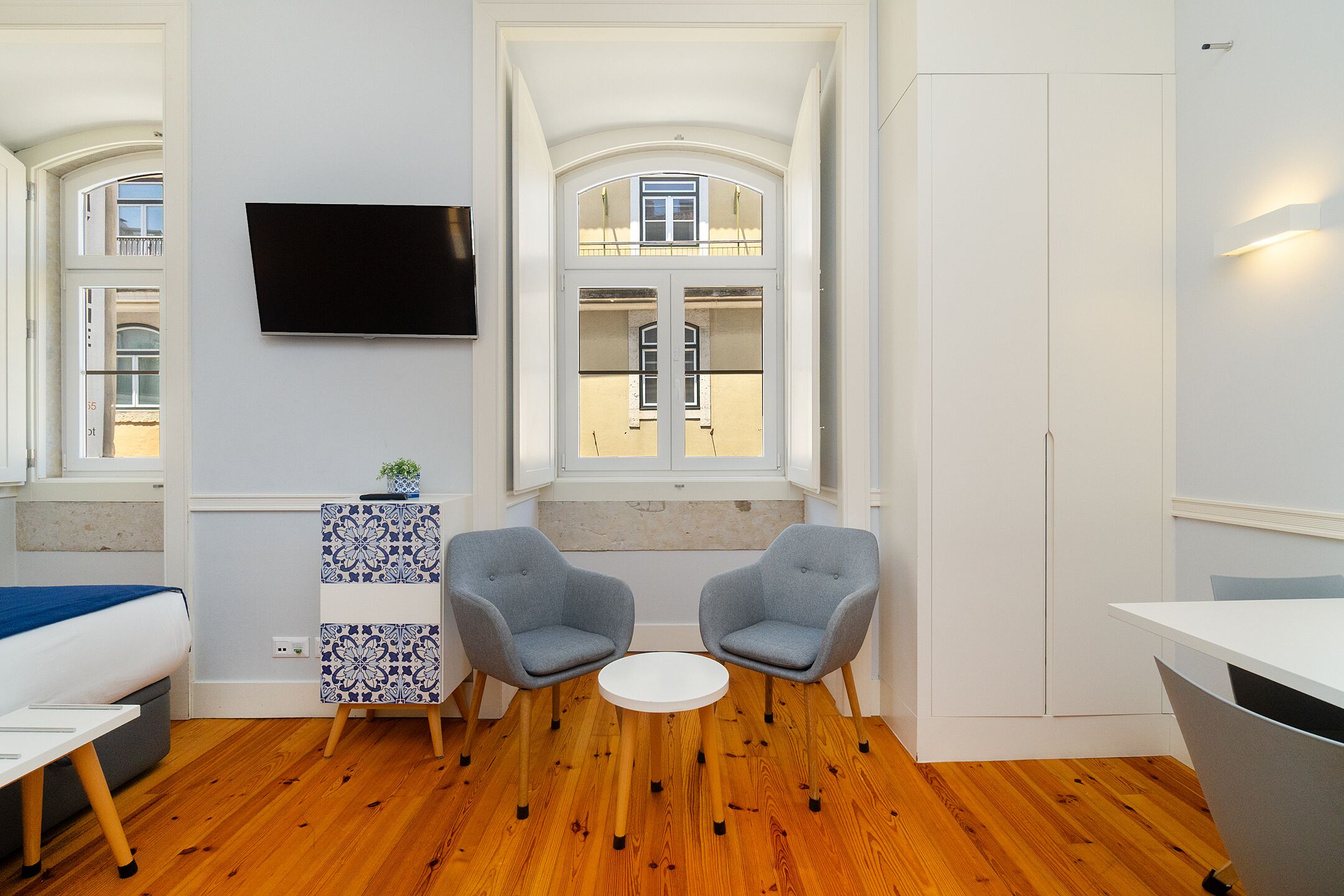 Een moderne kamer met een bed, twee fauteuils, een klein tafeltje, een televisie en grote ramen.
