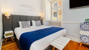 Un dormitorio moderno con una cama grande, lámparas de noche, televisión y ventana con vista a un edificio.