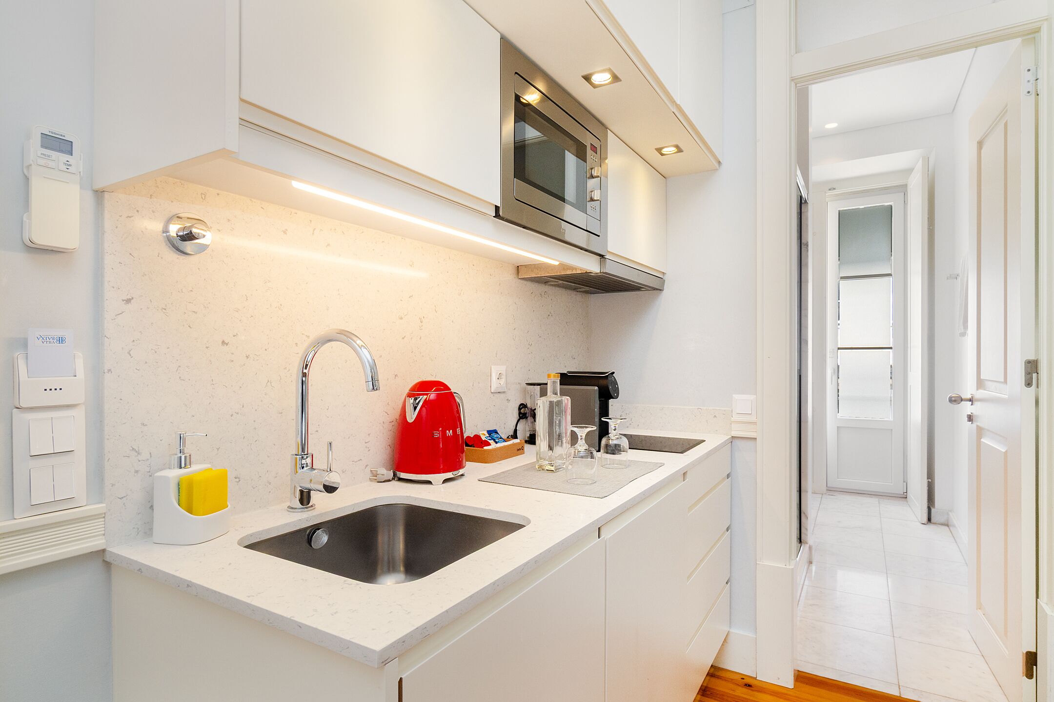 A modern kitchen with a double sink, stainless steel appliances, and a red kettle.