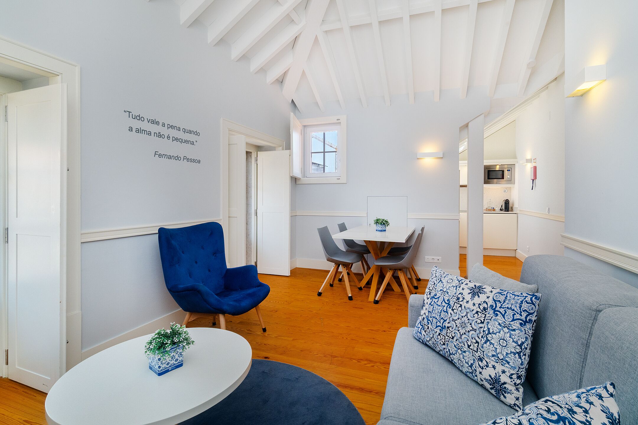 Un interno moderno con zona pranzo, una sedia blu, un divano grigio e una cucina sullo sfondo.