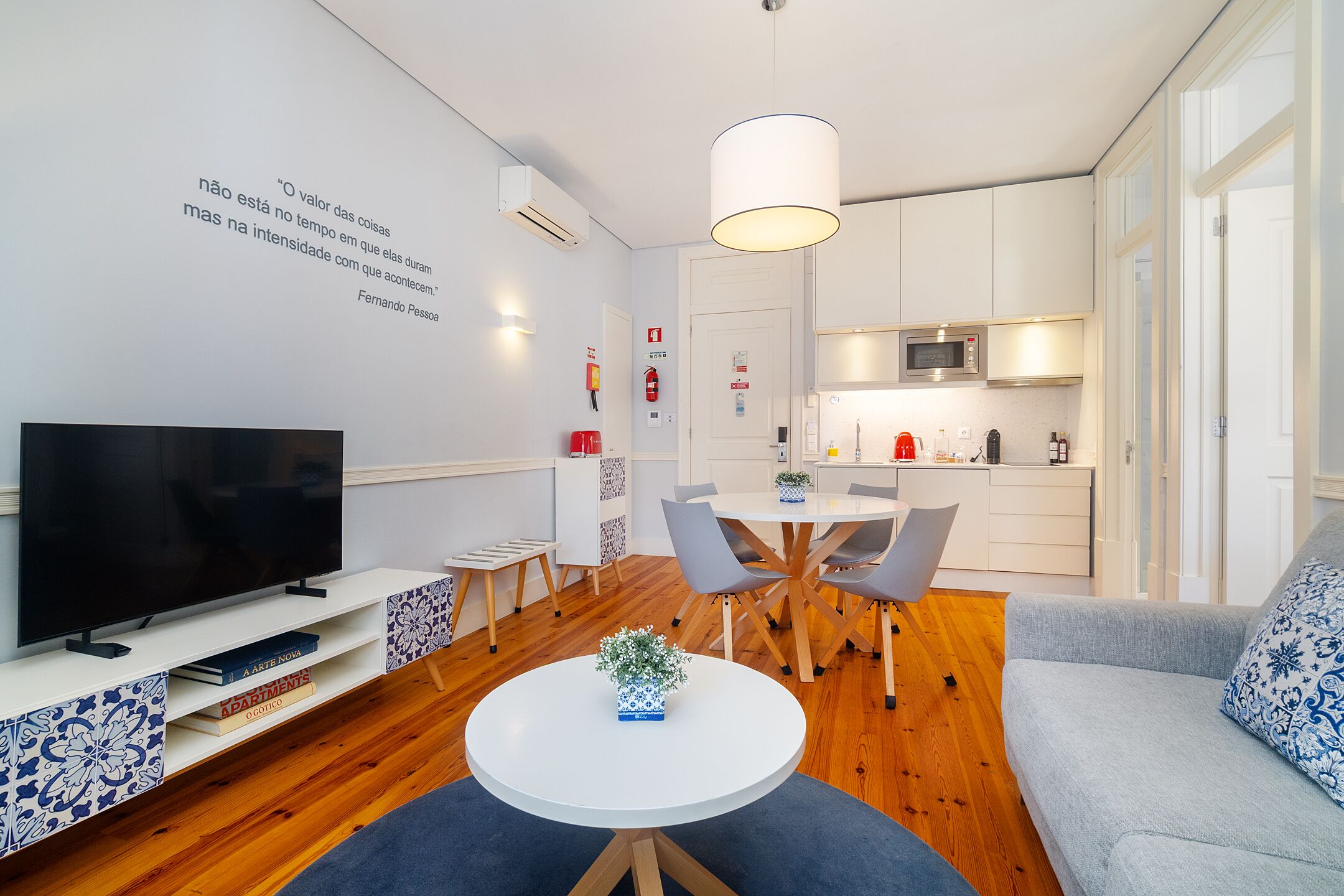 Una sala de estar moderna con un televisor de pantalla plana, una mesa de comedor con sillas, una mesa de centro con una planta y un sofá gris.
