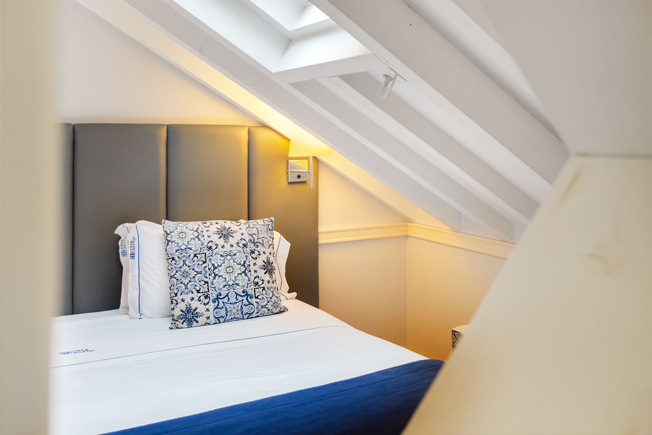 A bedroom with a sloped ceiling, a bed with a patterned pillow, and a wall-mounted light fixture.