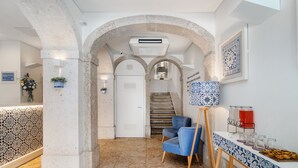Un vestíbulo de hotel con una recepción, una silla azul, un cuadro sobre caballete y una escalera.