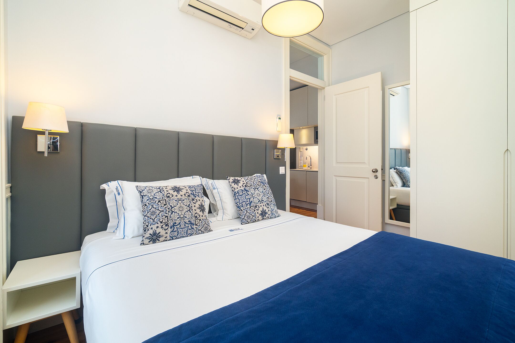 A neatly arranged bedroom with a bed, bedside lamps, and a visible bathroom door.