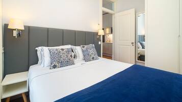 A neatly arranged bedroom with a bed, bedside lamps, and a visible bathroom door.
