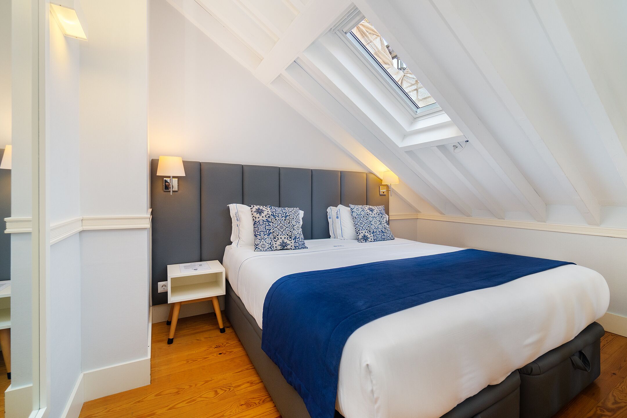 A bedroom with a skylight, a bed with a blue blanket, and a nightstand.
