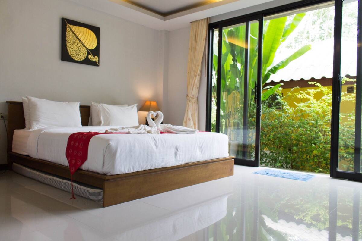 A bedroom with a large bed, a heart-shaped pillow, and a view of greenery outside.