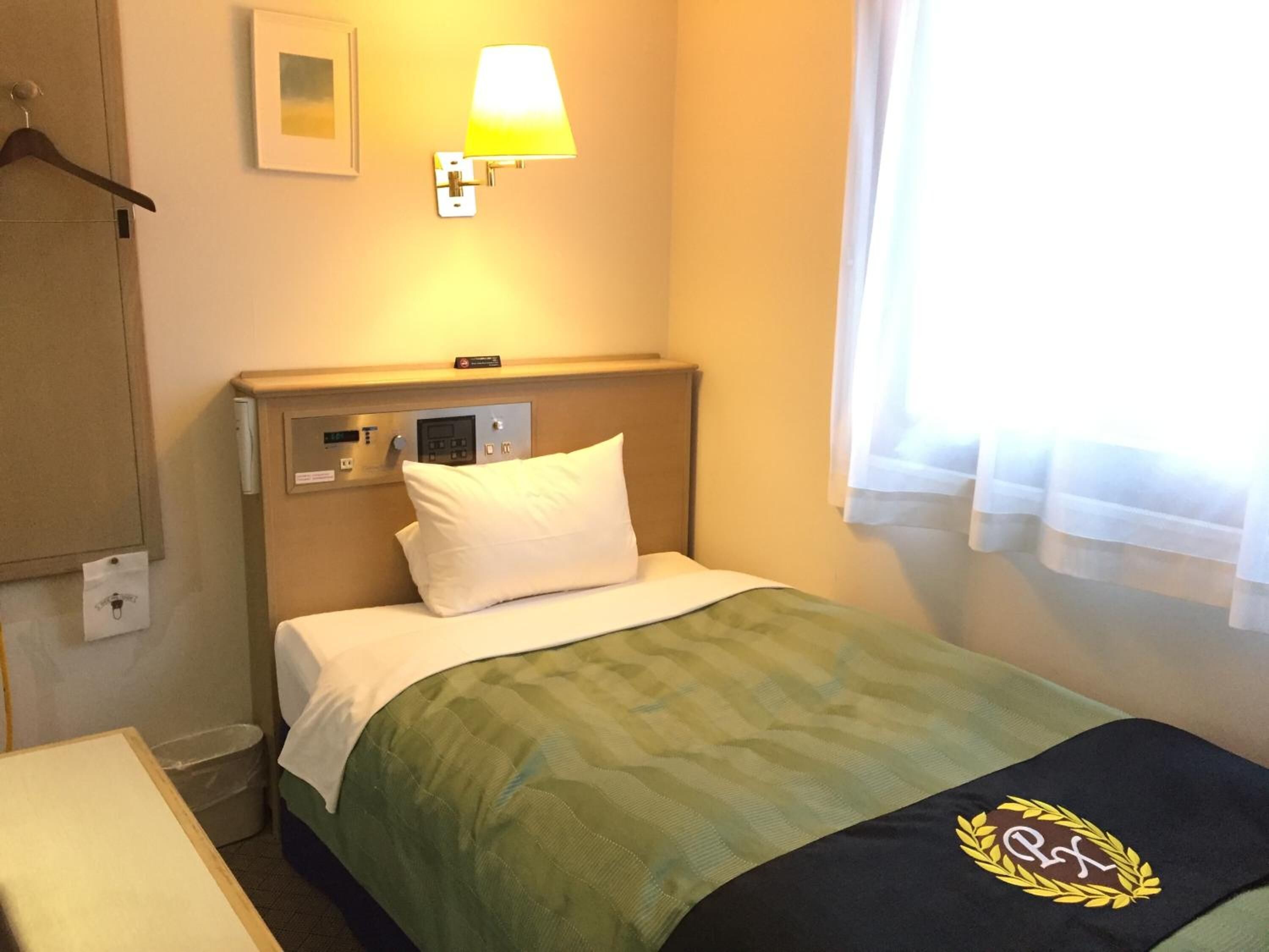 A hotel room with a bed, a control panel, a bedside lamp, a window with curtains, and a wall-mounted picture.