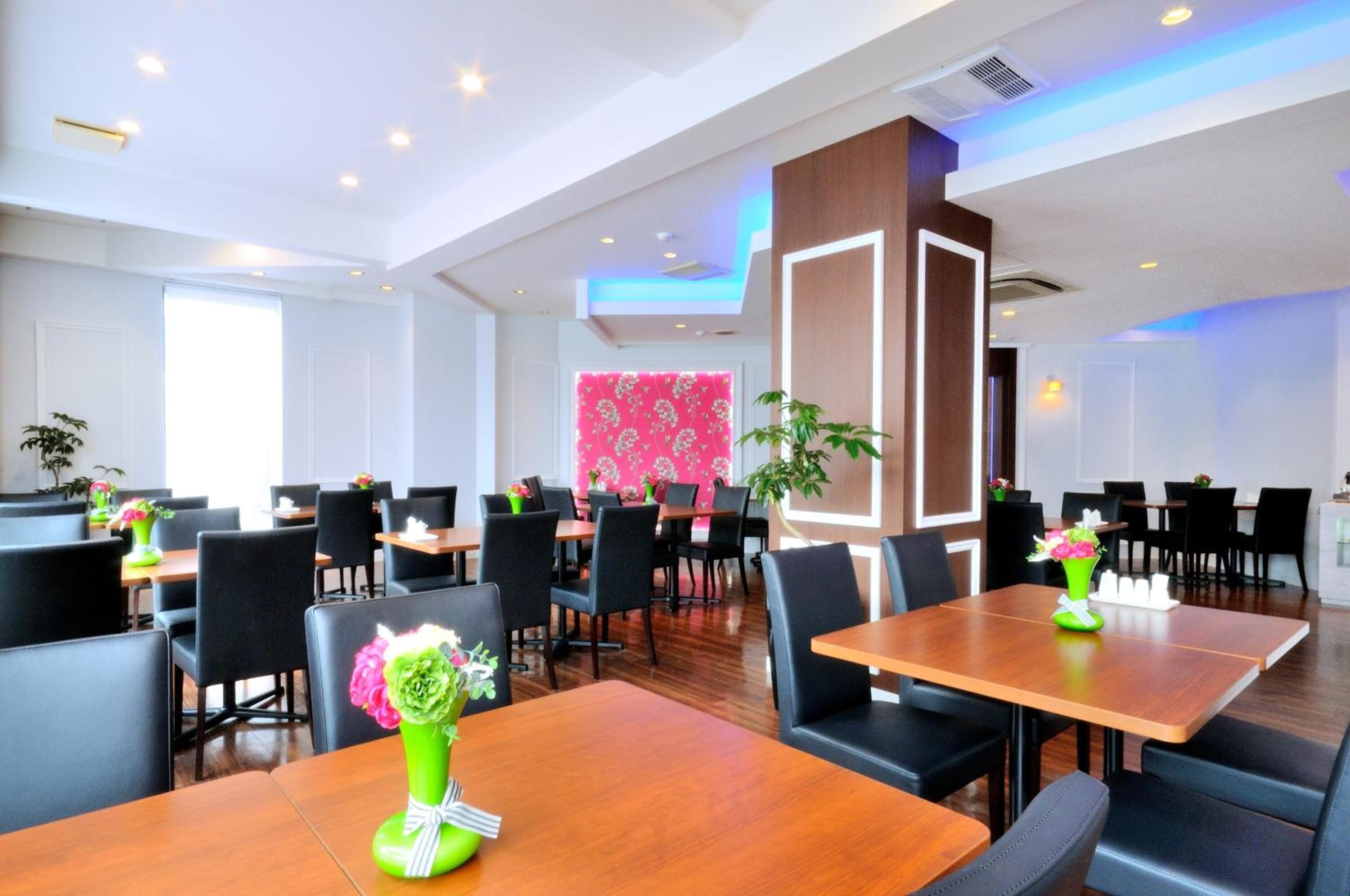 A modern dining area with wooden tables and black chairs, featuring a central decorative panel and potted plants.