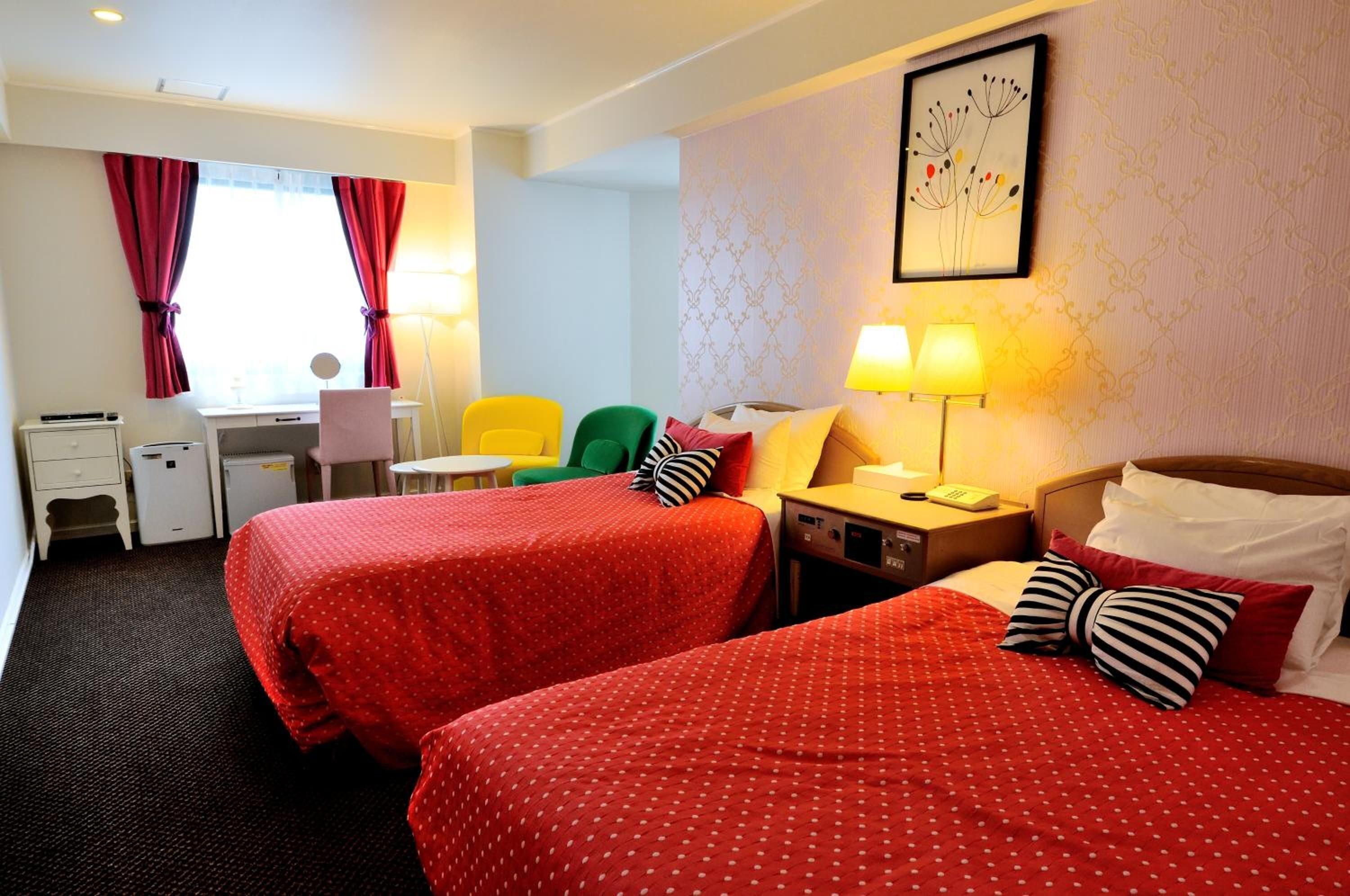 A hotel room with two beds, a desk, a chair, and a lamp.