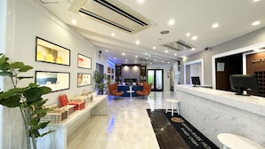 A hotel lobby with a reception desk, seating area, and a lounge in the background.