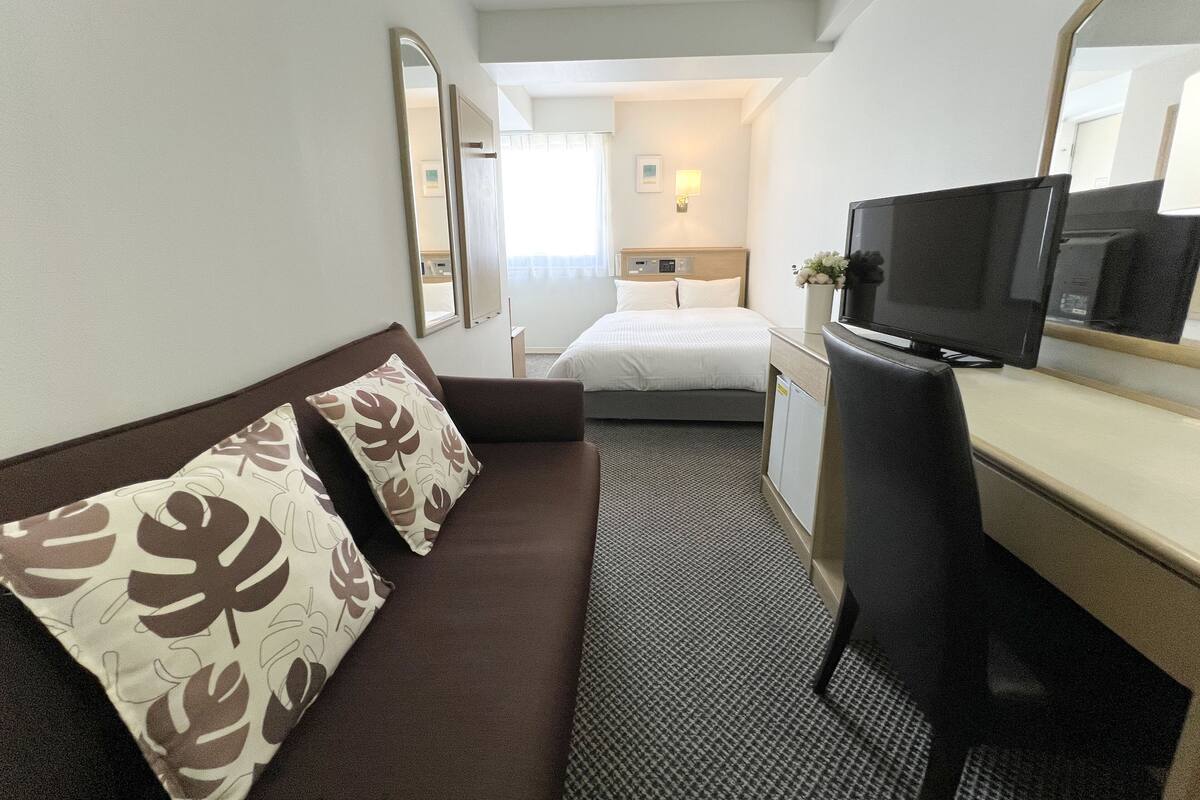 Een hotelkamer met een bruine bank, een bed, een televisie en een spiegel.