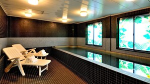 A spa room with a black tiled wall, a small pool, and two white chairs.