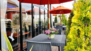 An outdoor patio with glass doors, red umbrellas, and potted plants.