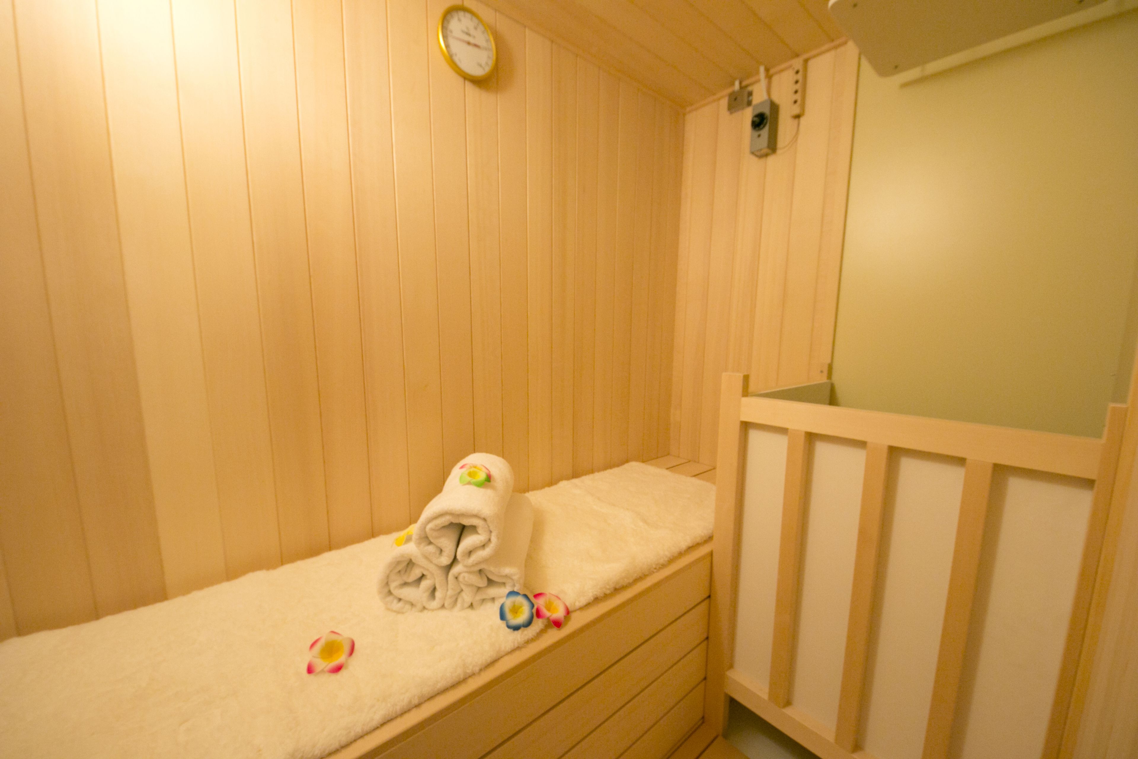 A wooden room with a single bed, a small bedside table, and a wall-mounted clock.