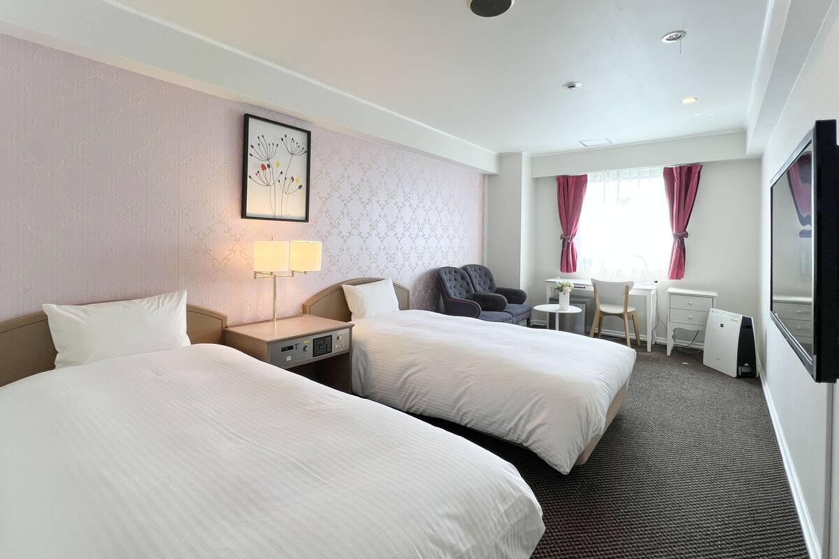 Een hotelkamer met twee bedden, een bureau, een stoel, een televisie en een raam met gordijnen.
