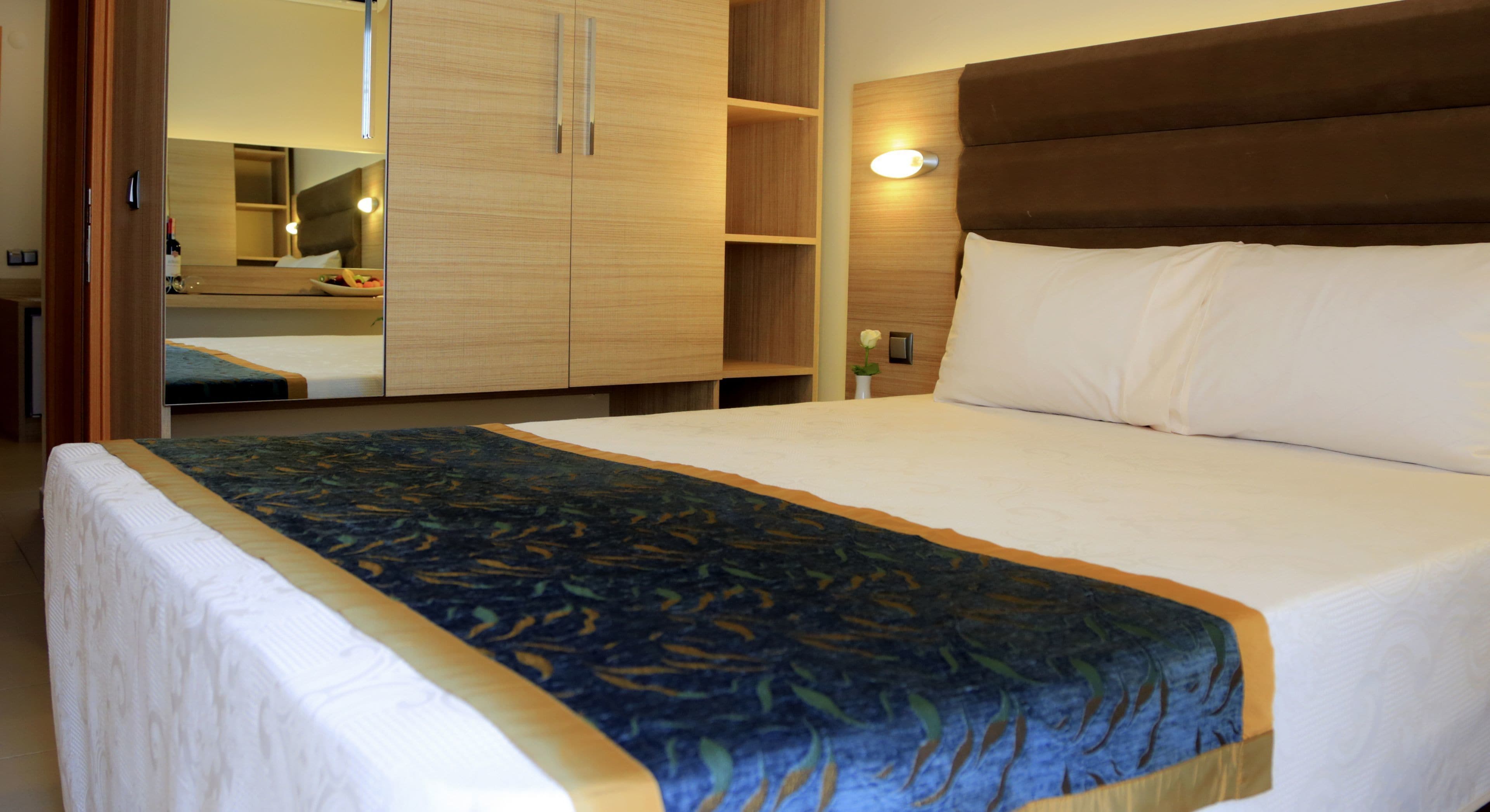 Een hotelkamer met een groot bed, een houten kledingkast en een nachtkastje met een lamp.