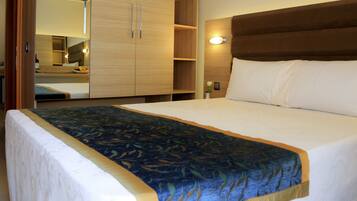 Een hotelkamer met een groot bed, een houten kledingkast en een nachtkastje met een lamp.