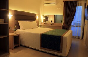 A hotel room with a large bed, bedside tables, a mirror, and an air conditioning unit.