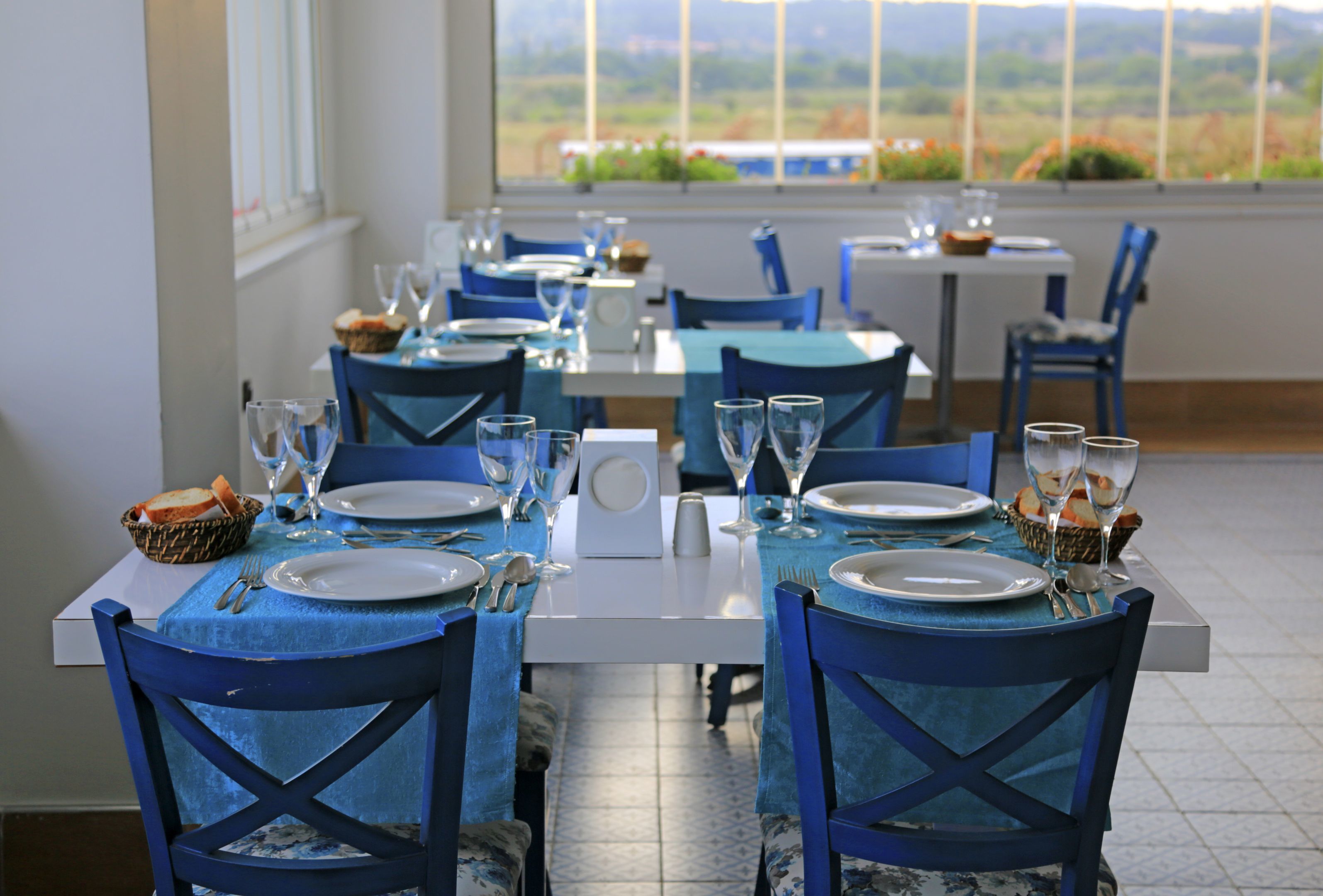 A dining area with tables set for two, chairs, and a view of the outdoors.